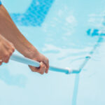 Cleaner of the swimming pool . Man in a blue shirt with cleaning equipment for swimming pools, sunny.