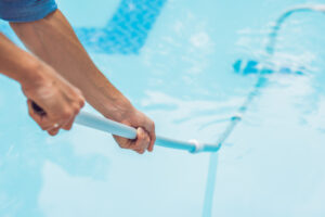 Cleaner of the swimming pool . Man in a blue shirt with cleaning equipment for swimming pools, sunny.