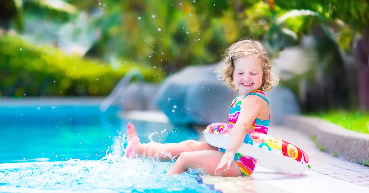 happy little girl sitting on side of pool splashing her feet in the water